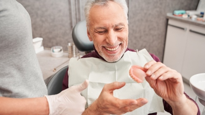 Smiling senior man in dental chair holding a denture