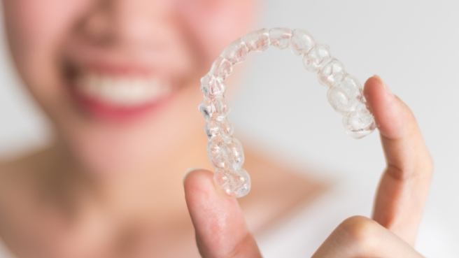 Smiling person holding Invisalign in Irving