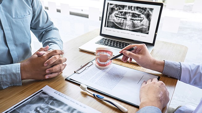 a dentist pointing at a model of a mouth while speaking to a patient