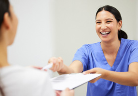 a dental staff member handing a patient forms on a clipboard