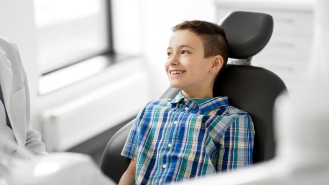 Young boy in plaid shirt grinning in dental chair