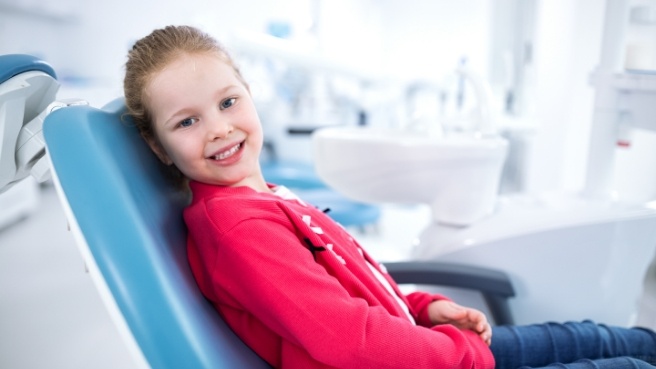 Young girl in red shirt smiling in dental chair