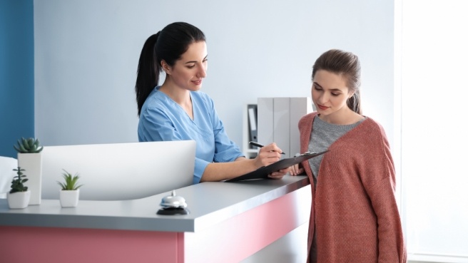 Dental receptionist showing a patient where to sign on clipboard