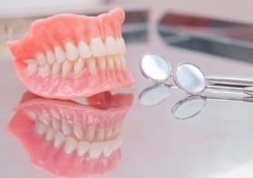 Full dentures resting on table with dental mirrors
