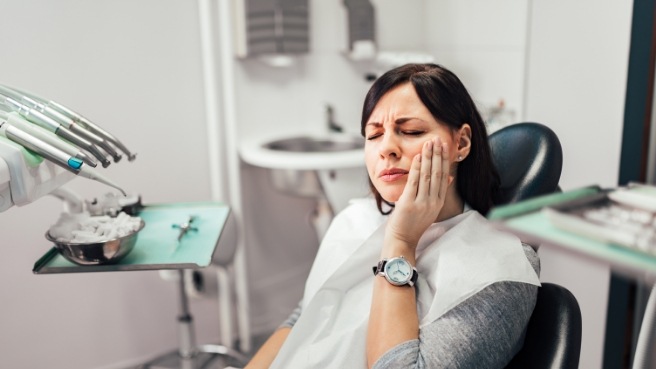 Woman holding her cheek in pain while visiting emergency dentist in Irving