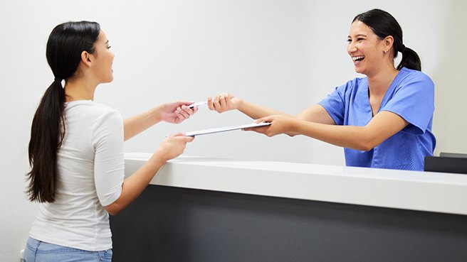 a front desk worker handing a patient forms