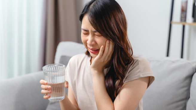 a woman drinking a glass of water and experiencing dental sensitivity
