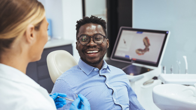 : a dentist speaking with a patient sitting in a treatment chair