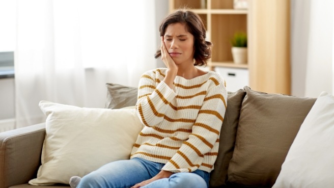 Woman on couch holding her cheek in pain