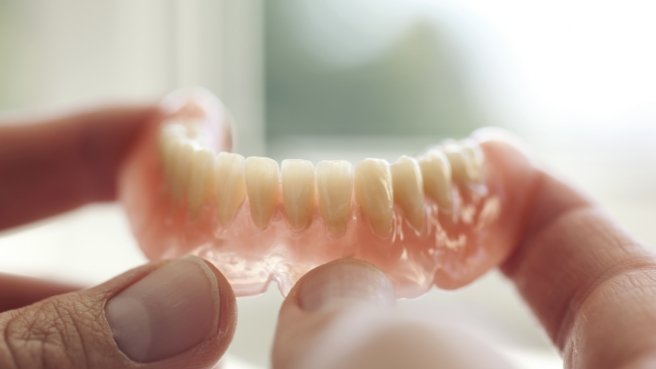 Person holding full denture in their hands