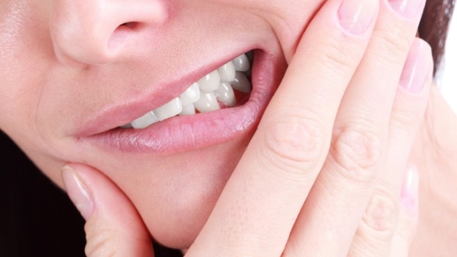 Person holding their cheek in pain before tooth extractions in Irving