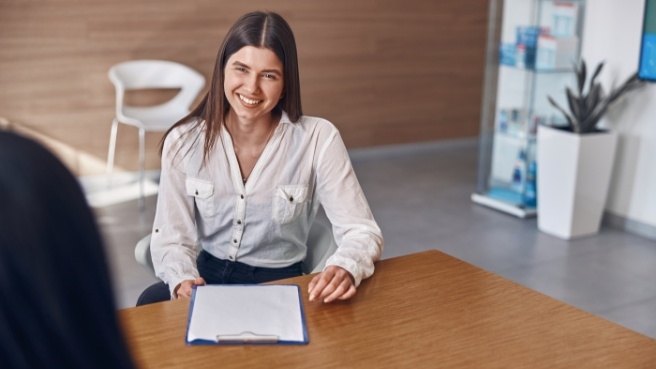 Smiling woman with clipboard sitting at desk