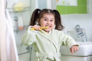 a child smiling and brushing their teeth in the bathroom