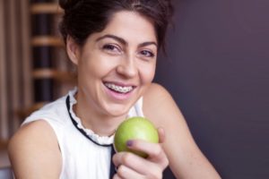  a person who has braces smiling and holding an apple