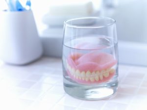 dentures soaking in a glass of denture cleaner on a bathroom counter