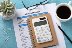 a calculator and monthly budget sheet next to a cup of coffee on a table