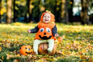 a smiling child dressed as a pumpkin sitting outside