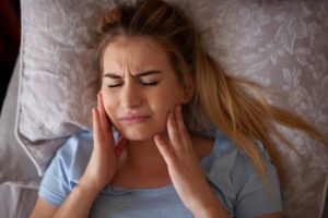 a person grinding their teeth and holding their jaw while laying in bed