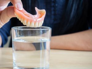 a person placing dentures in a glass of water