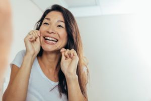 person flossing their teeth while looking in a bathroom mirror