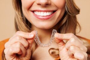 a smiling woman holding a clear aligner