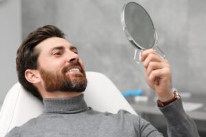 a man looking in a handheld mirror at his new dental crown