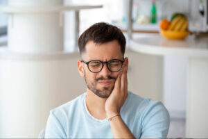 a man wearing glasses holding his mouth because he has a toothache