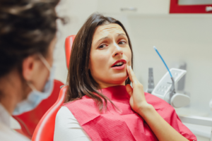 a woman holding her cheek in pain while speaking with a dentist