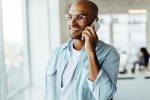 a man with glasses speaking on the phone and smiling